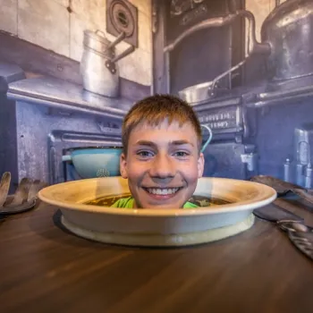 Jongen lacht met zijn hoofd door een tafel in een optische illusie-attractie in Limburg.