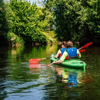 Twee mensen kajakken met een kajak van Schurenhof over de smalle rivier de Roer, omringd door groen en bomen.