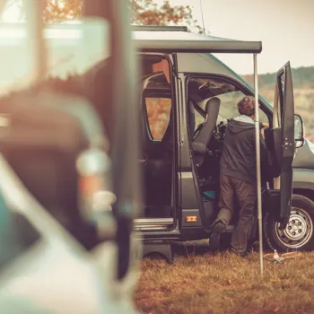 Camper met open deur op een grasveld, terwijl iemand instapt voor een reis door de natuur.